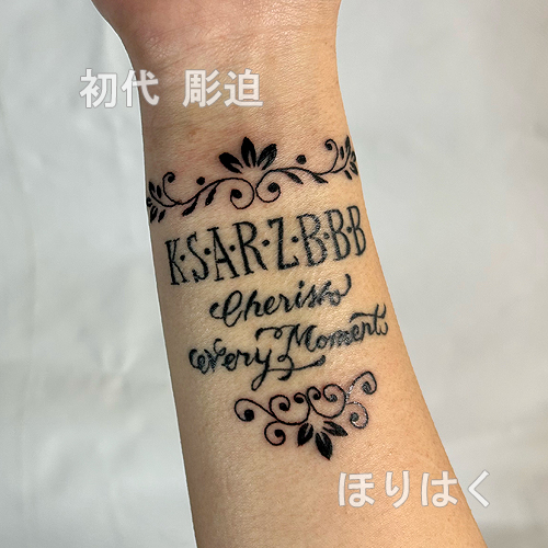 アルファベットと筆記体のデザインの周りに唐草模様のタトゥー